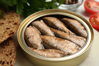 Photo of Tin can with tasty sprats served on board, closeup