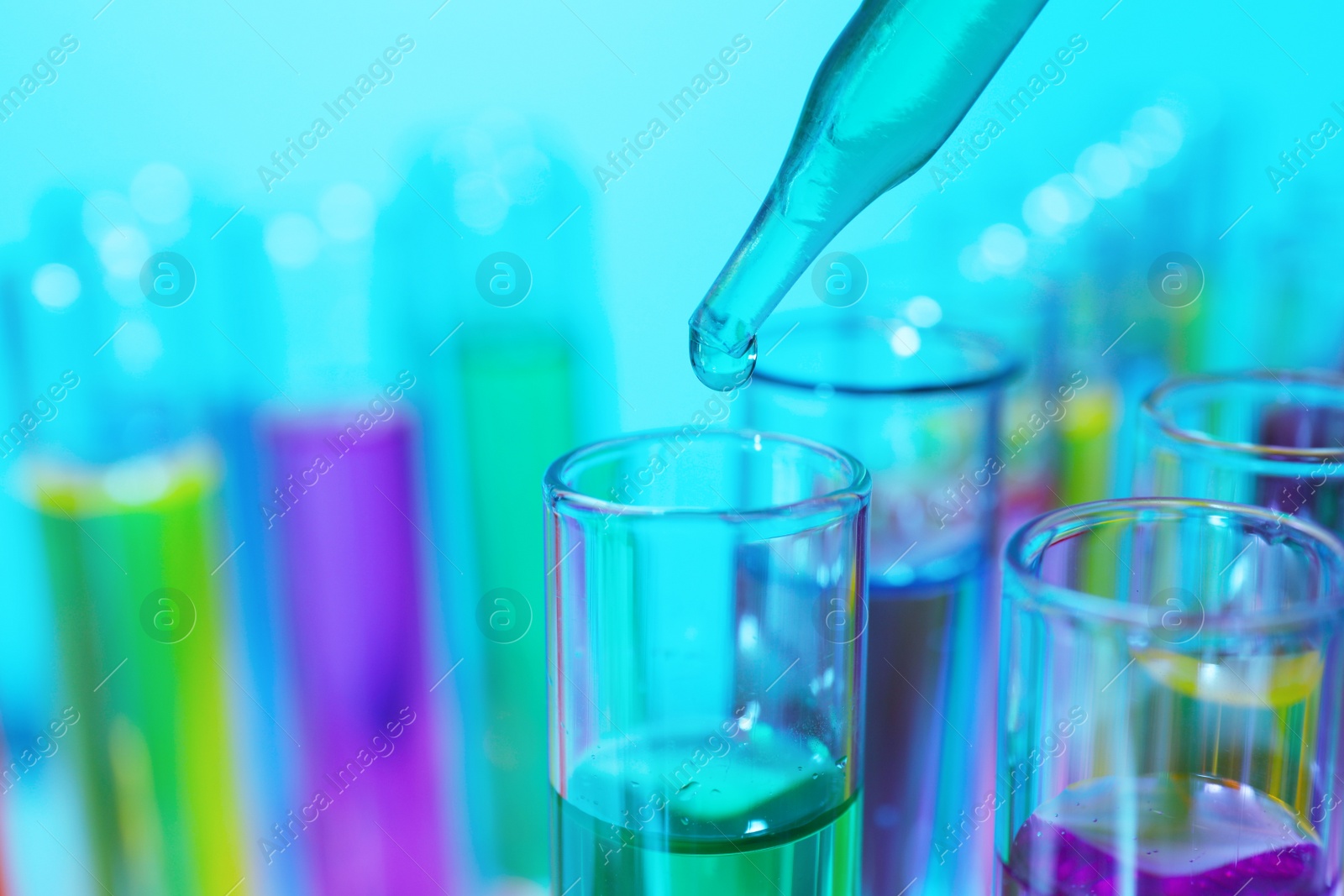 Photo of Dripping liquid from pipette into test tube on light blue background, closeup