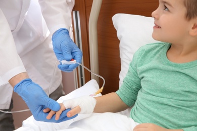 Doctor adjusting intravenous drip for little child in hospital, closeup