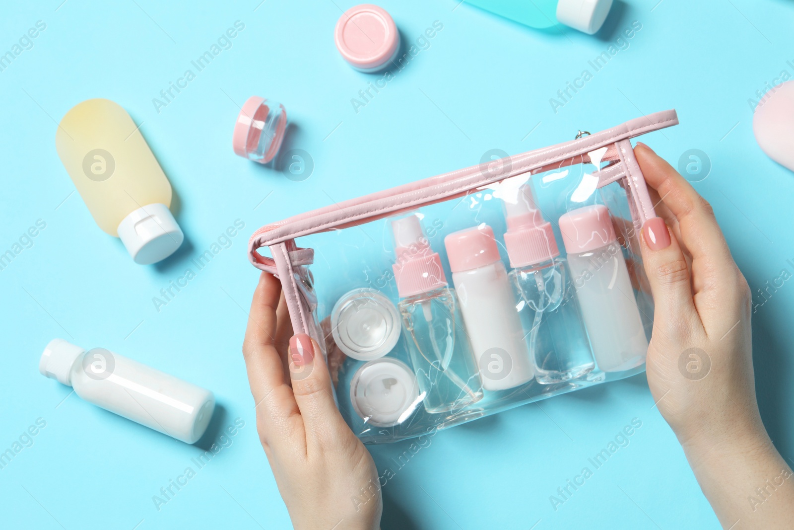 Photo of Cosmetic travel kit. Woman with plastic bag and small containers of personal care products on light blue background, top view