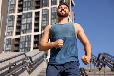 Photo of Happy man running down stairs outdoors on sunny day, low angle view