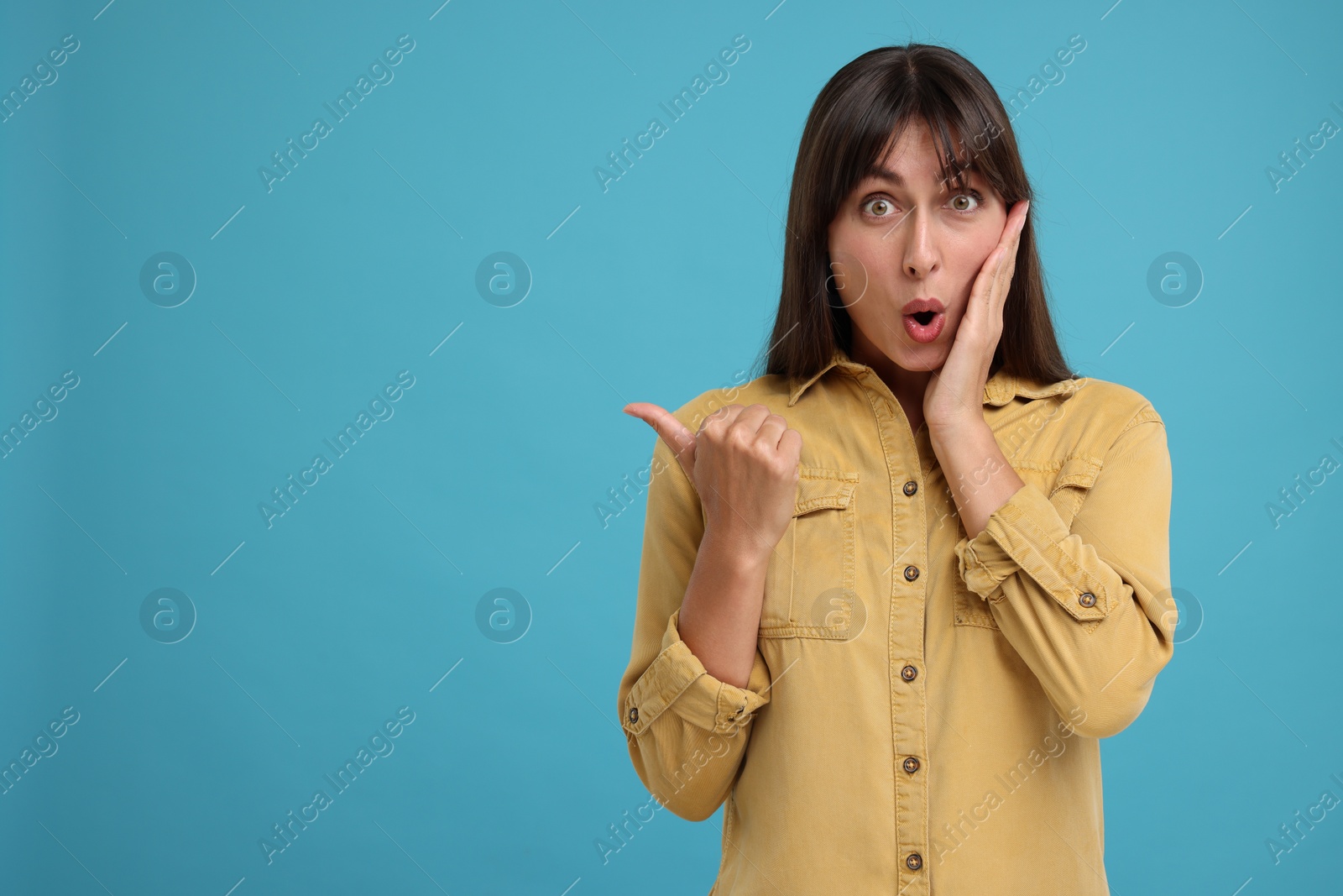 Photo of Special promotion. Surprised woman pointing at something on light blue background, space for text