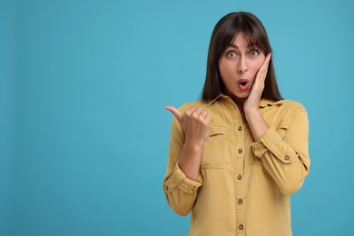 Photo of Special promotion. Surprised woman pointing at something on light blue background, space for text