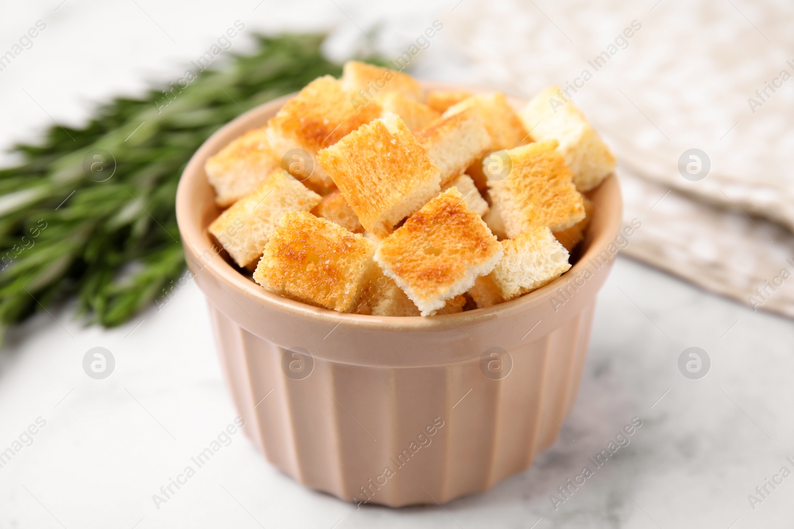 Photo of Delicious crispy croutons in bowl on white marble table, closeup