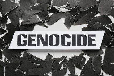 Card with word Genocide and pieces of torn black paper on white background, flat lay
