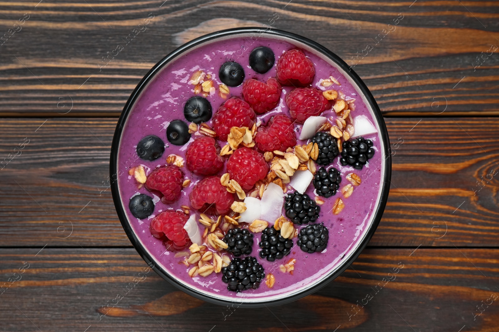 Photo of Delicious acai smoothie with berries and oatmeal on wooden table, top view