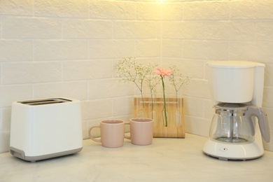 Photo of Modern toaster, cups, flowers and coffee machine on counter in kitchen