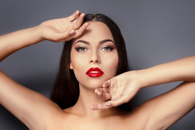 Portrait of beautiful young woman with red glossy lips on gray background