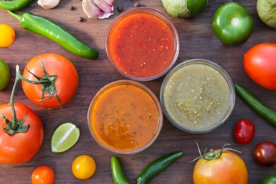 Photo of Tasty salsa sauces and ingredients on wooden table, flat lay
