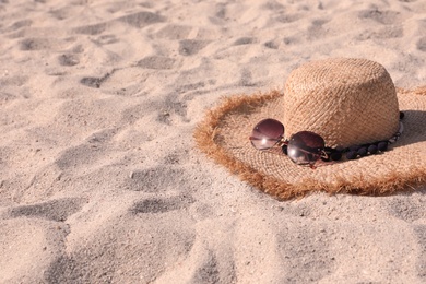 Photo of Straw hat with sunglasses on sandy beach. Space for text