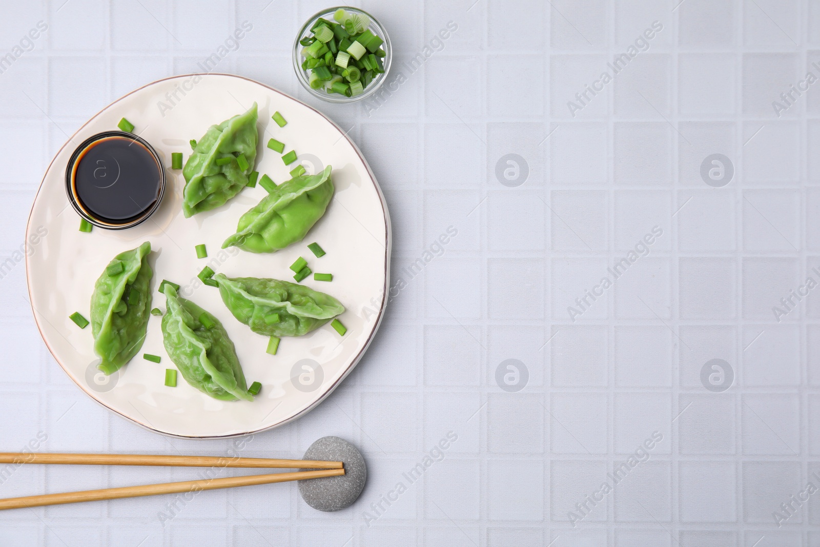 Photo of Delicious green dumplings (gyozas) served on white tiled table, flat lay. Space for text