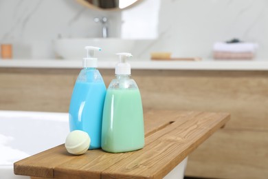 Photo of Wooden tray with bottles of shower gels and bath bomb on tub indoors, space for text