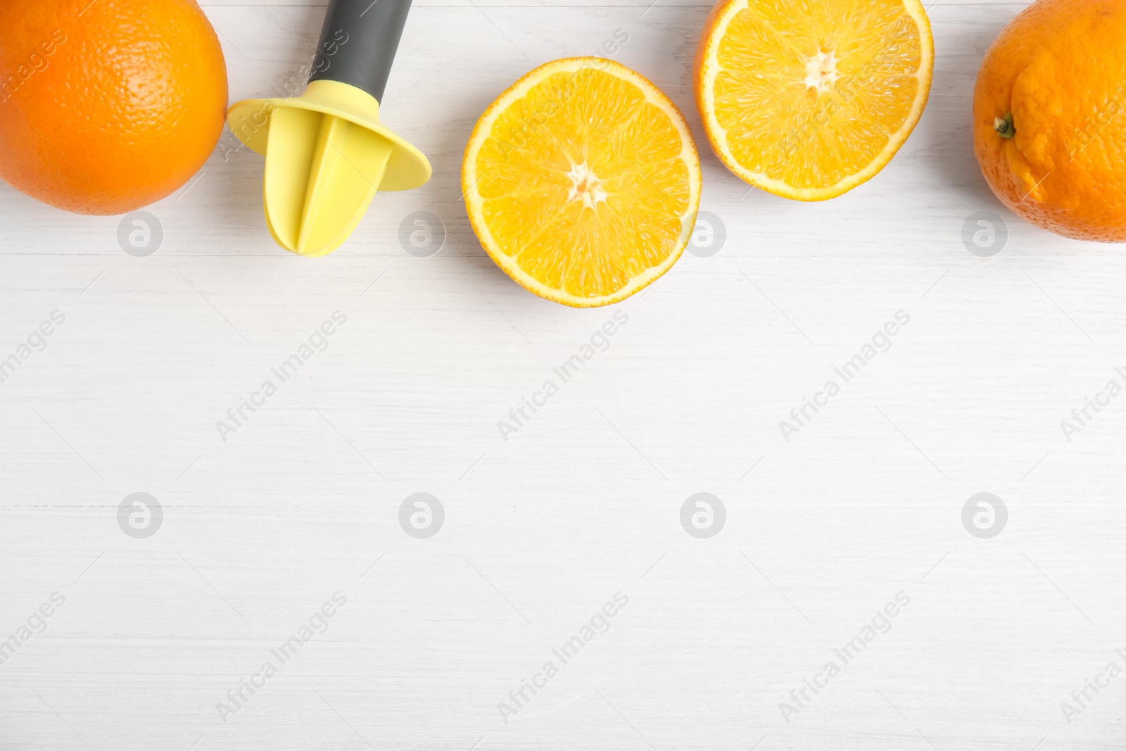 Photo of Fresh ripe oranges and reamer on white wooden table, flat lay. Space for text