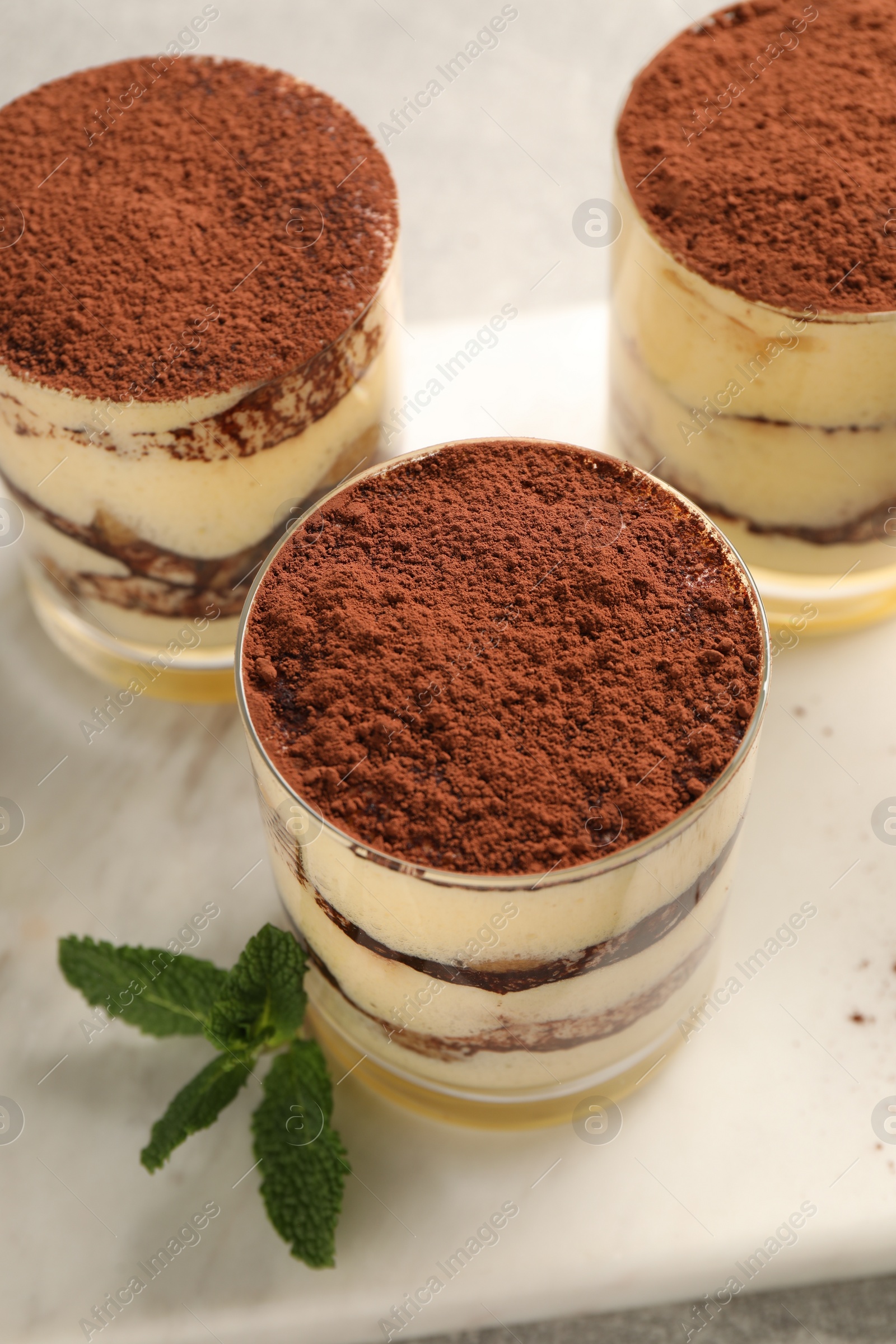 Photo of Delicious tiramisu in glasses and mint on table, above view