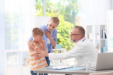 Photo of Coughing little boy with mother visiting doctor at clinic