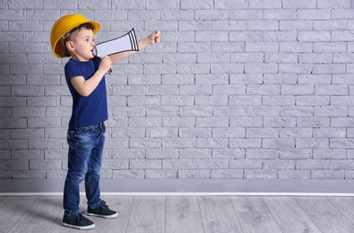 Adorable little boy in hardhat with paper megaphone on brick wall background