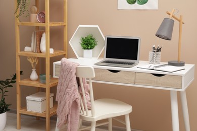 Photo of Cozy workplace with modern laptop on desk and comfortable chair at home