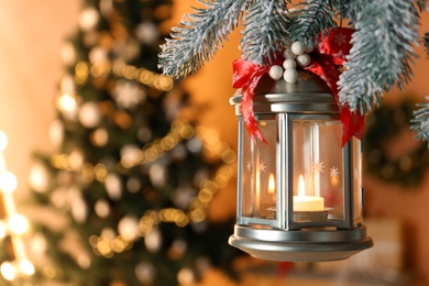 Photo of Vintage Christmas lantern with burning candle hanging on fir branch against blurred background. Space for text