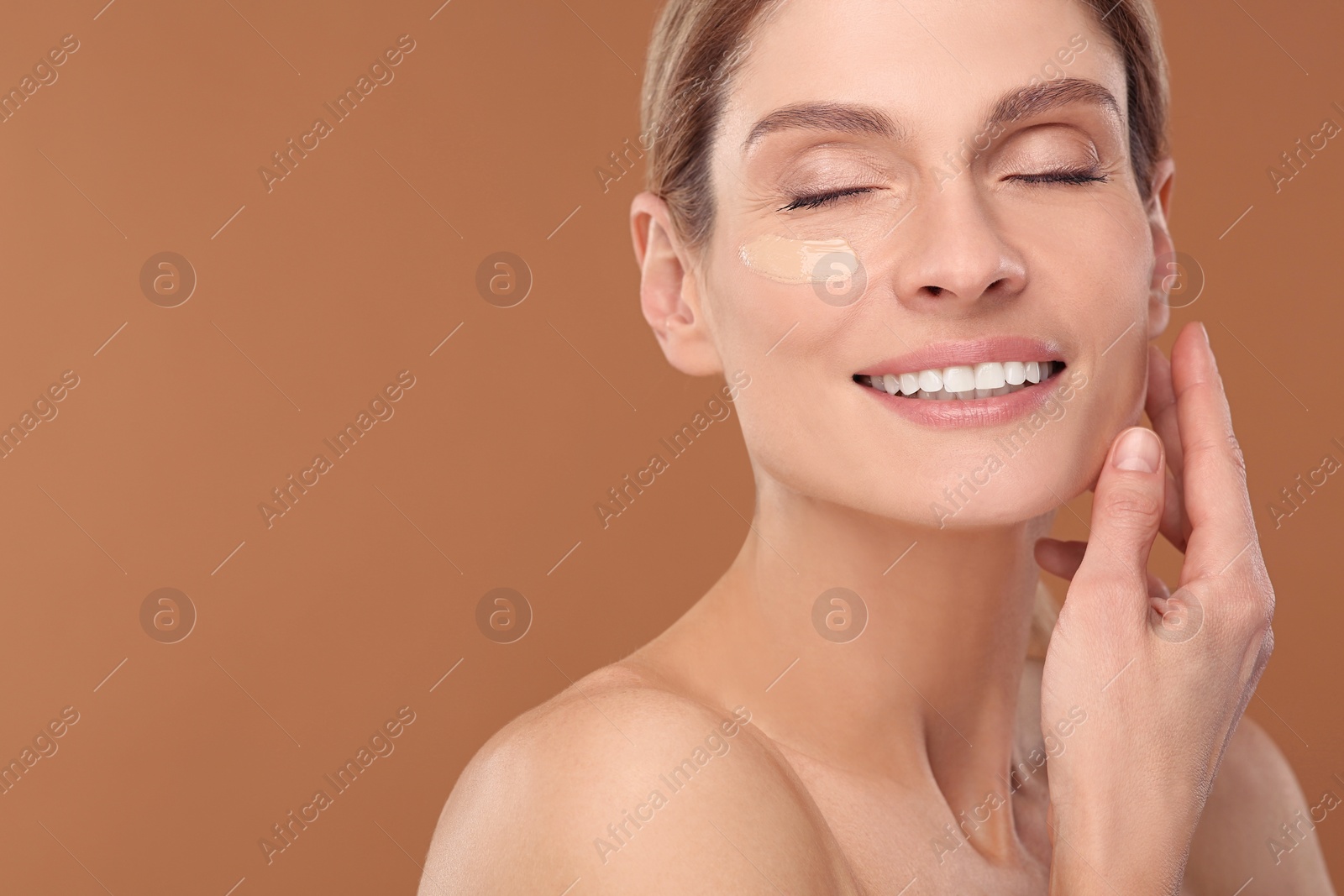 Photo of Woman with swatch of foundation on face against brown background. Space for text