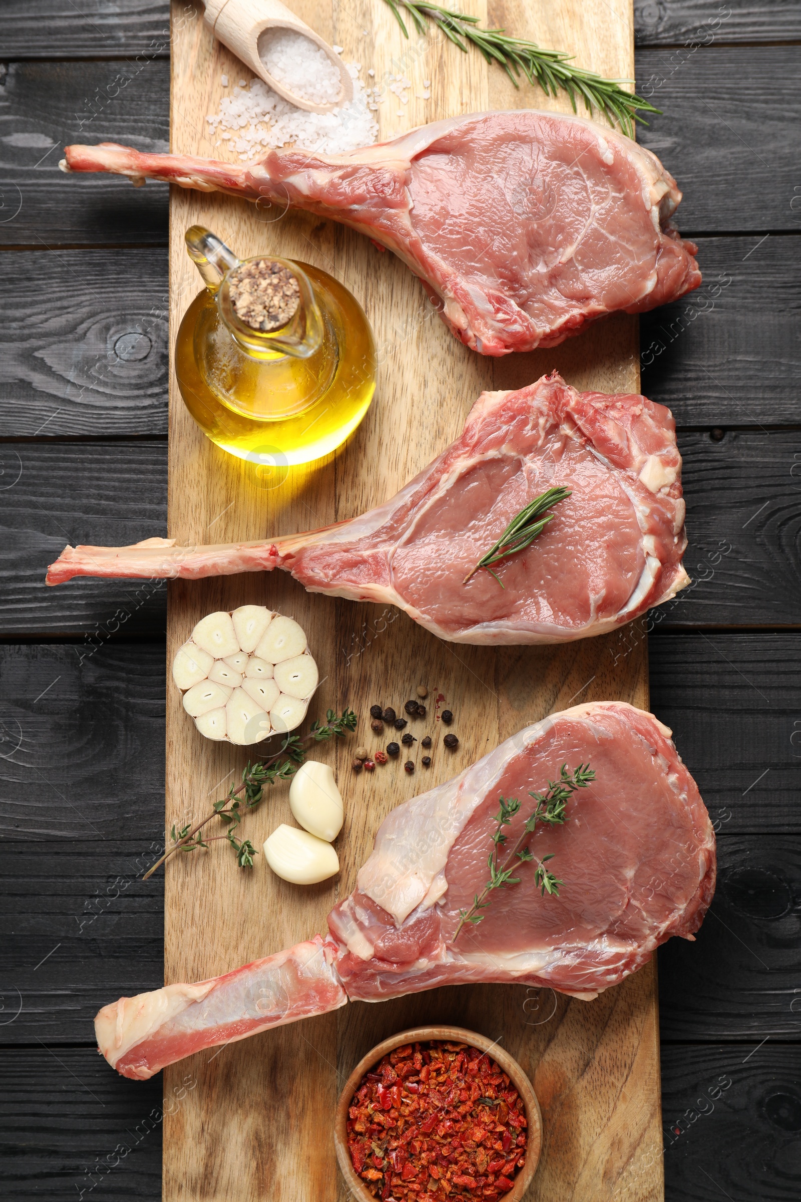 Photo of Fresh tomahawk beef cuts, spices and oil on black wooden table, top view