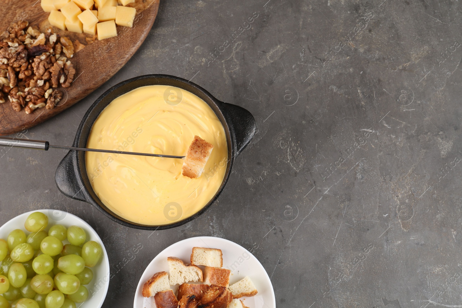 Photo of Fondue pot with tasty melted cheese, fork and different snacks on grey table, flat lay. Space for text