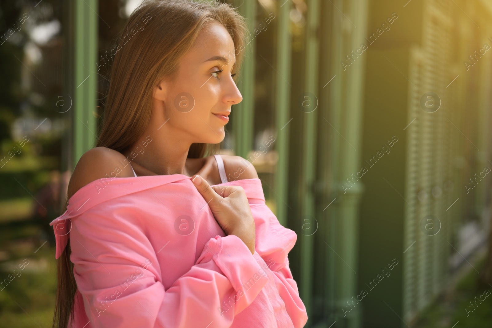 Photo of Beautiful young woman in stylish pink shirt near building outdoors, space for text