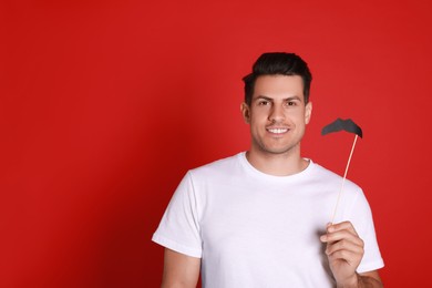 Photo of Happy man with fake mustache on red background