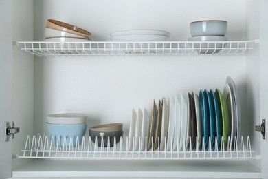 Photo of Different clean plates and bowls on shelves in cabinet