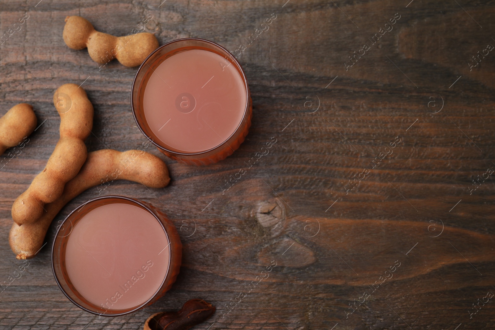 Photo of Tamarind juice and fresh fruits on wooden table, flat lay. Space for text