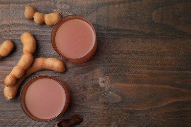 Photo of Tamarind juice and fresh fruits on wooden table, flat lay. Space for text