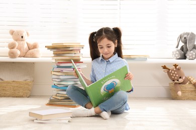 Little girl reading book on floor at home