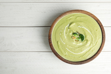 Photo of Delicious broccoli cream soup served on white wooden table, top view. Space for text