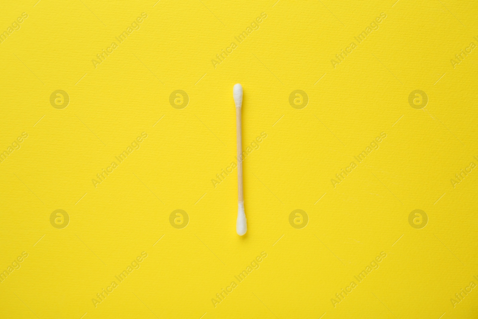 Photo of One wooden cotton bud on yellow background, top view