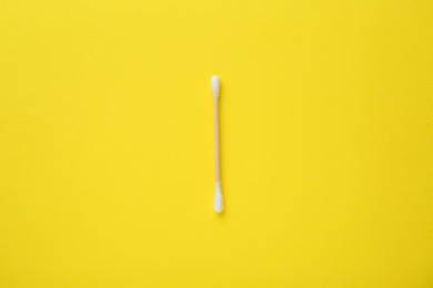 Photo of One wooden cotton bud on yellow background, top view