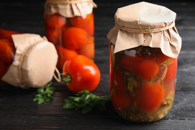 Pickled tomatoes in glass jars on black wooden table