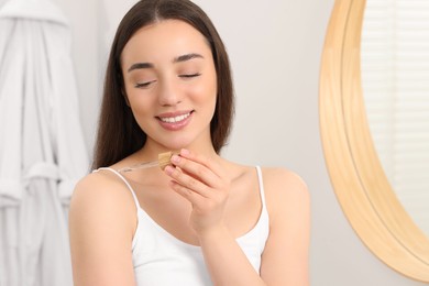 Woman applying essential oil onto shoulder in bathroom, closeup