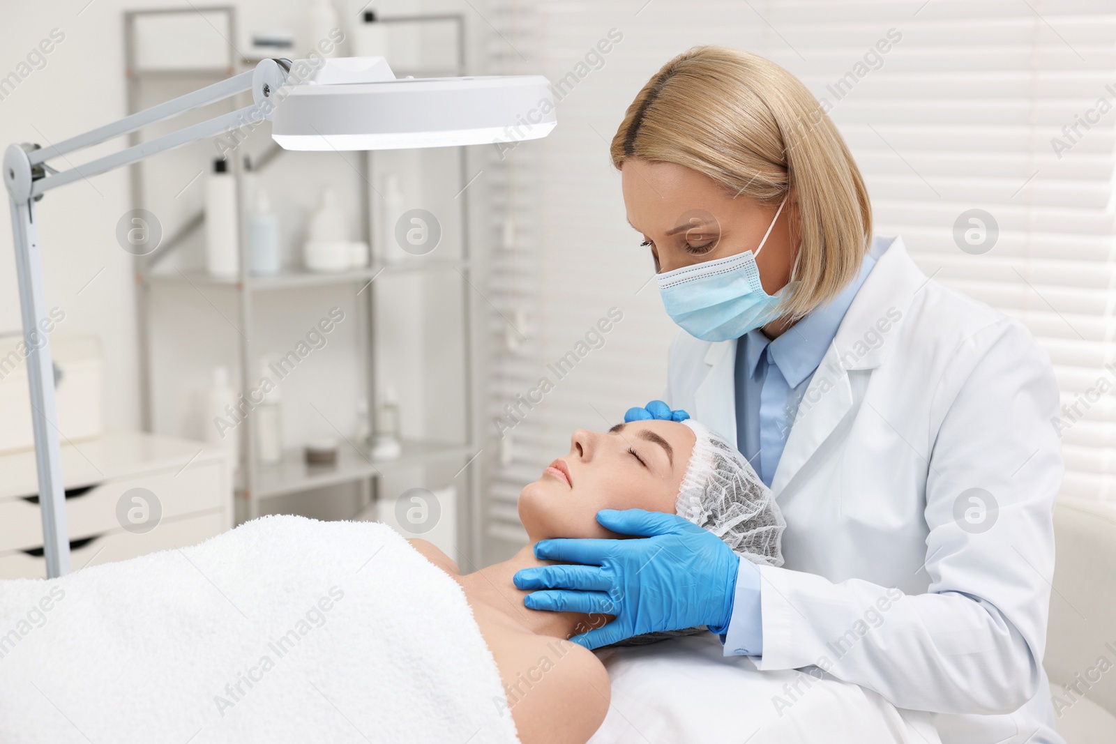 Photo of Dermatologist examining patient`s face under lamp in clinic