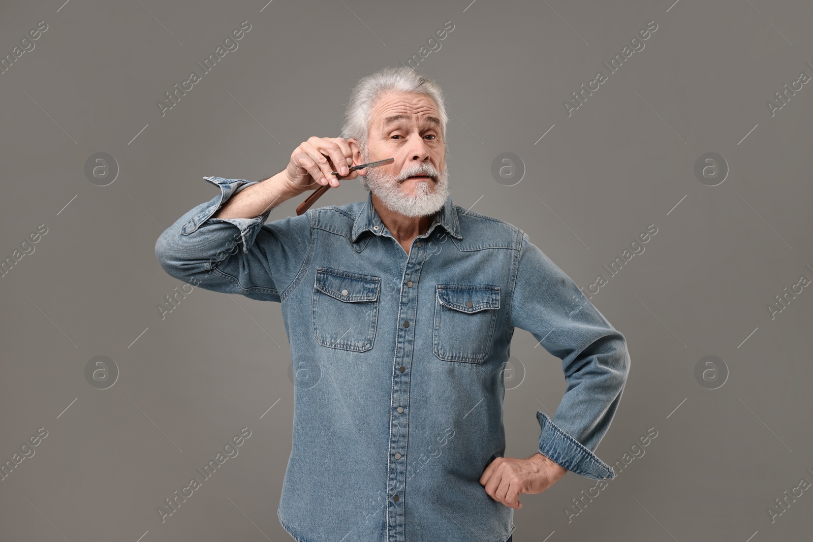 Photo of Senior man shaving beard with blade on grey background