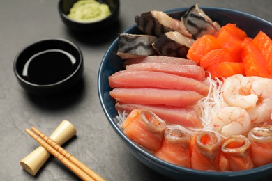 Photo of Delicious mackerel, salmon, shrimps and tuna served with funchosa, soy sauce and wasabi on grey table, closeup. Tasty sashimi dish
