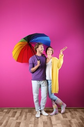 Couple with rainbow umbrella near color wall