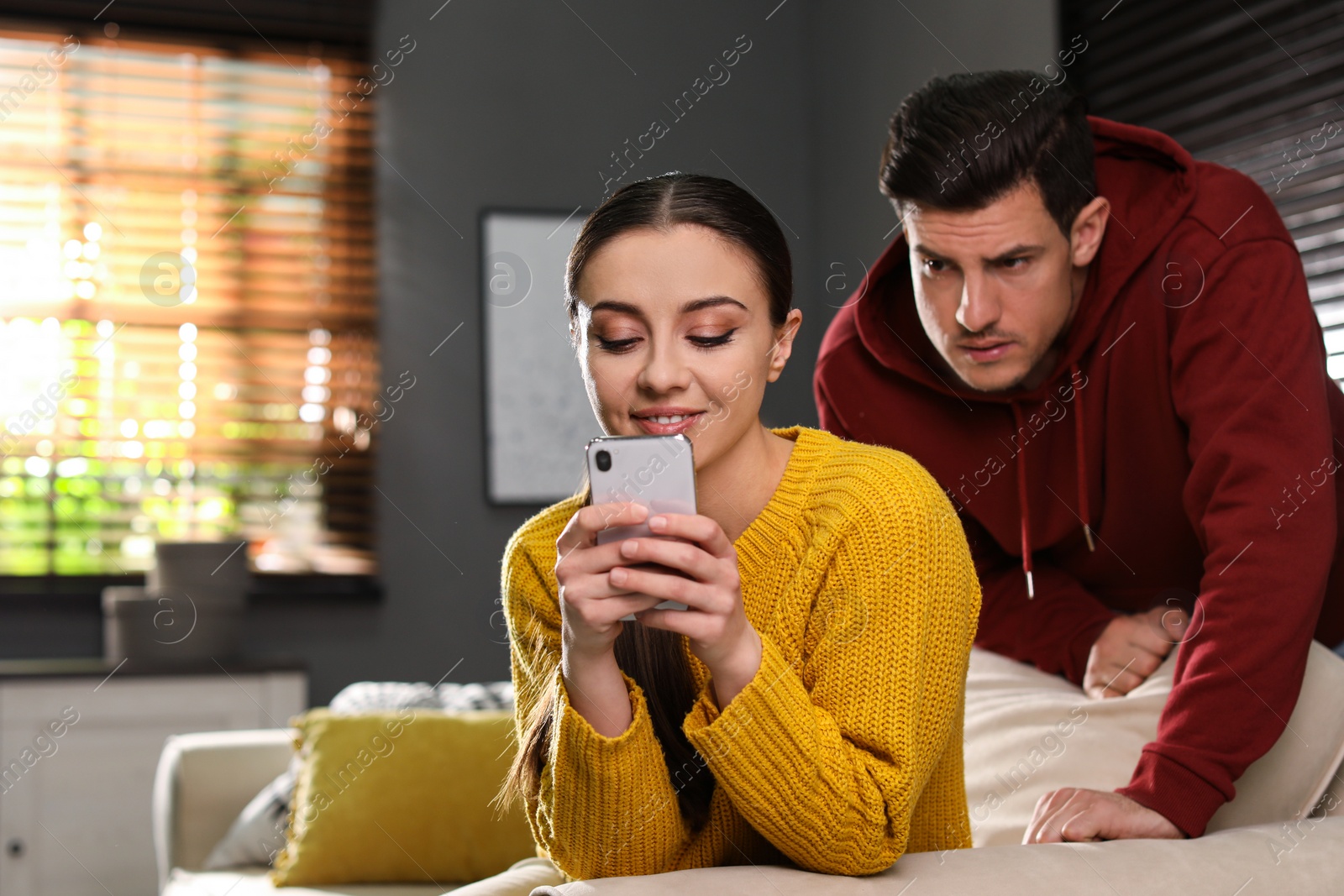 Photo of Distrustful man peering into girlfriend's smartphone at home. Jealousy in relationship