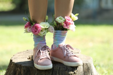 Photo of Woman standing on wooden stump outdoors with flowers in socks, closeup
