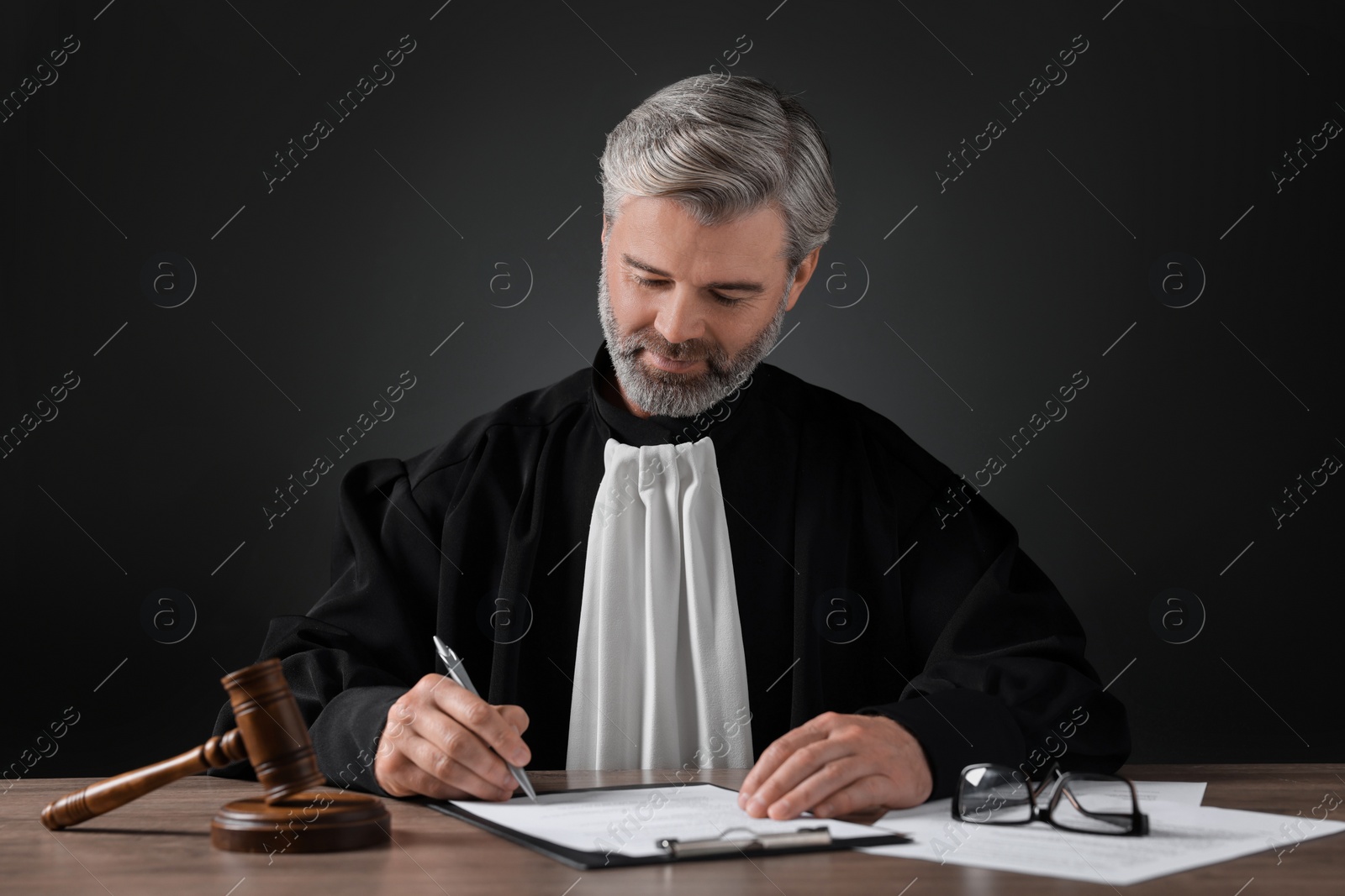 Photo of Judge working with documents at wooden table against black background