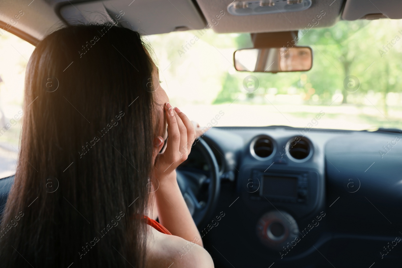 Photo of Happy young beautiful woman looking in rear mirror inside car