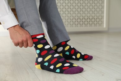 Photo of Man putting on colorful socks indoors, closeup