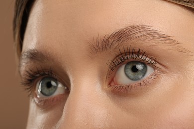 Woman with long eyelashes after mascara applying against light brown background, closeup