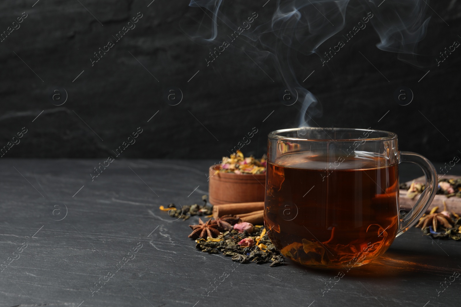 Photo of Glass cup of freshly brewed tea and dry leaves on black table. Space for text