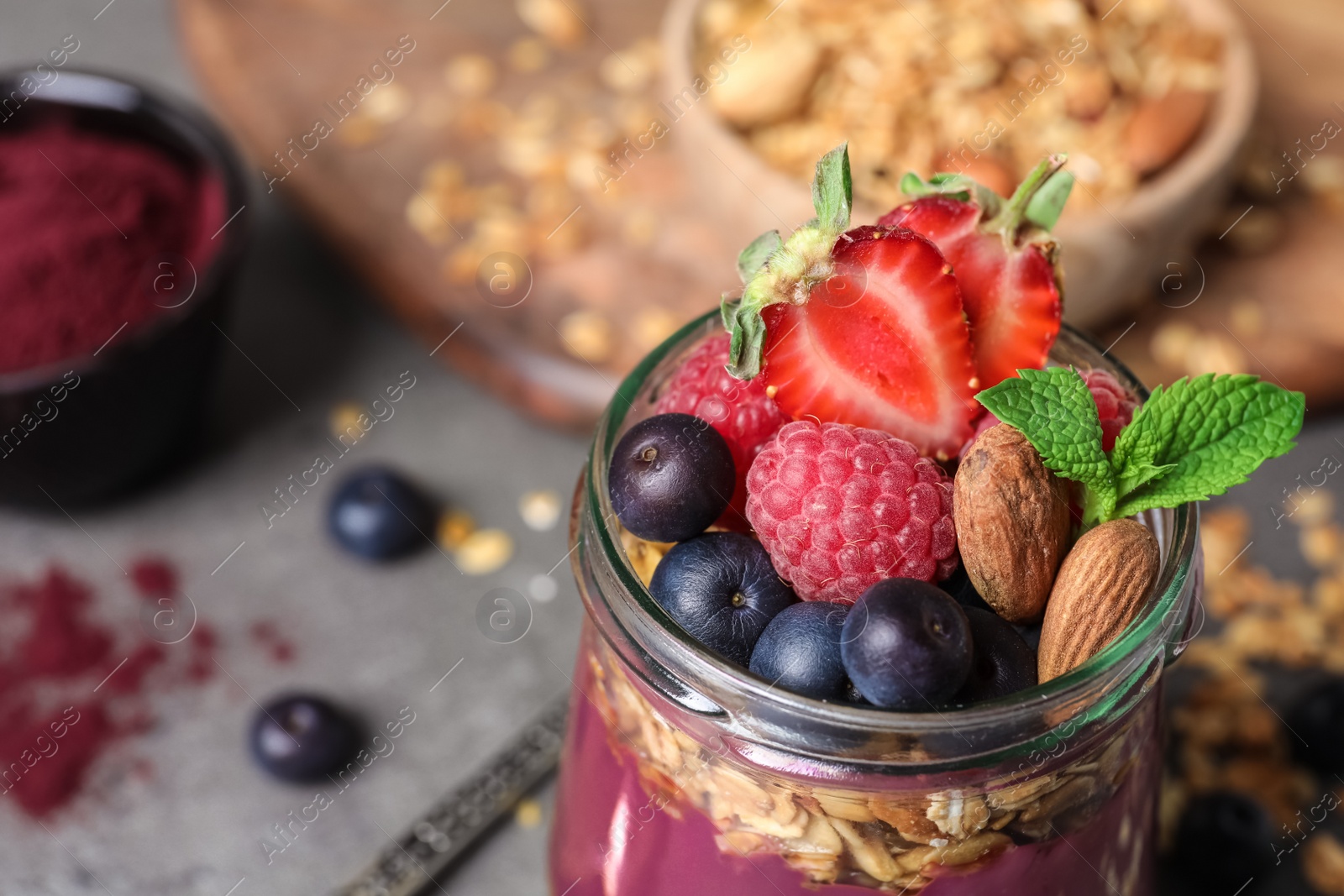 Photo of Delicious acai dessert with granola and berries served on grey table, closeup