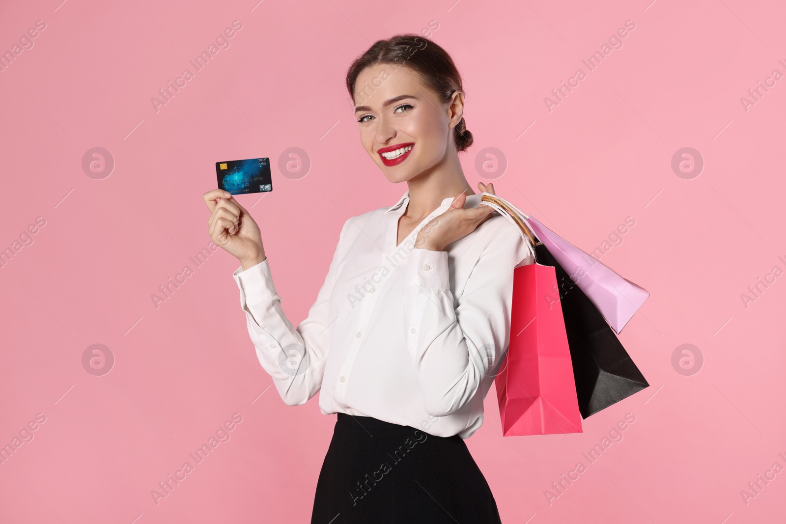 Photo of Happy young woman with shopping bags and credit card on light pink background. Big sale