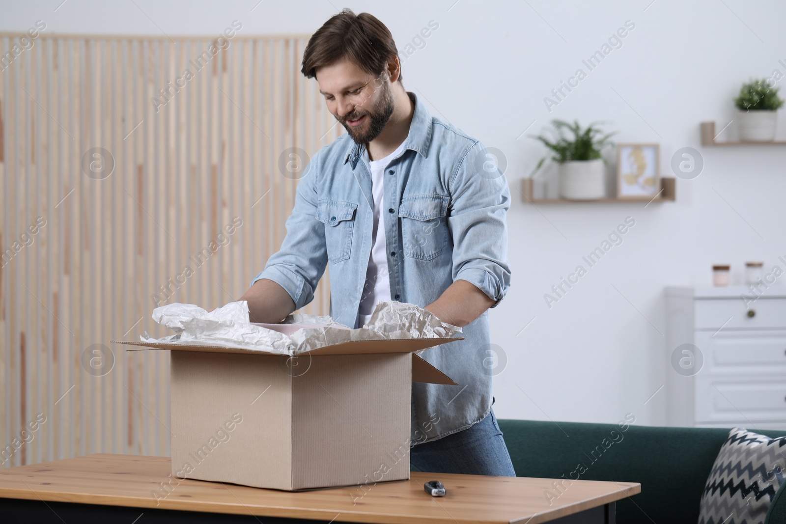 Photo of Happy man opening parcel at home. Internet shopping